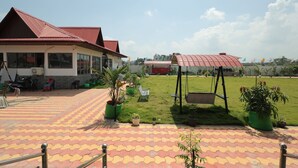 A courtyard with a tiled floor, a building with a red roof, and a swing set. - LUIT BLUE HOMESTAY & RESORTS (Guwahati)