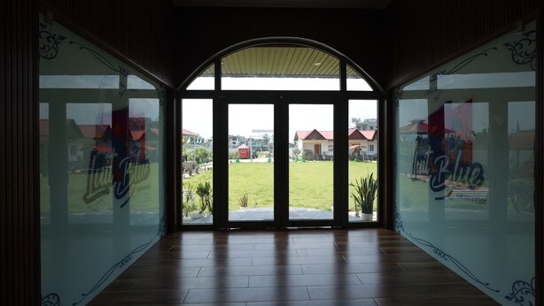A hotel room with large windows, a wooden floor, and a view of the outside. - LUIT BLUE HOMESTAY & RESORTS (Guwahati)