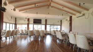 A spacious dining area with wooden flooring, white upholstered chairs, and pendant lighting. - LUIT BLUE HOMESTAY & RESORTS (Guwahati)
