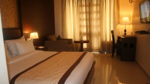 Habitación de hotel con una cama grande, un escritorio, una silla, una mesita y un televisor en la pared.