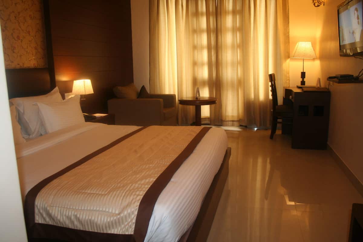 Habitación de hotel con una cama grande, un escritorio, una silla, una mesita y un televisor en la pared.
