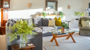 A living room with a sofa, coffee table, and a clock. - Fairway, Thorpeness, Aldeburgh, Suffolk (Thorpeness)