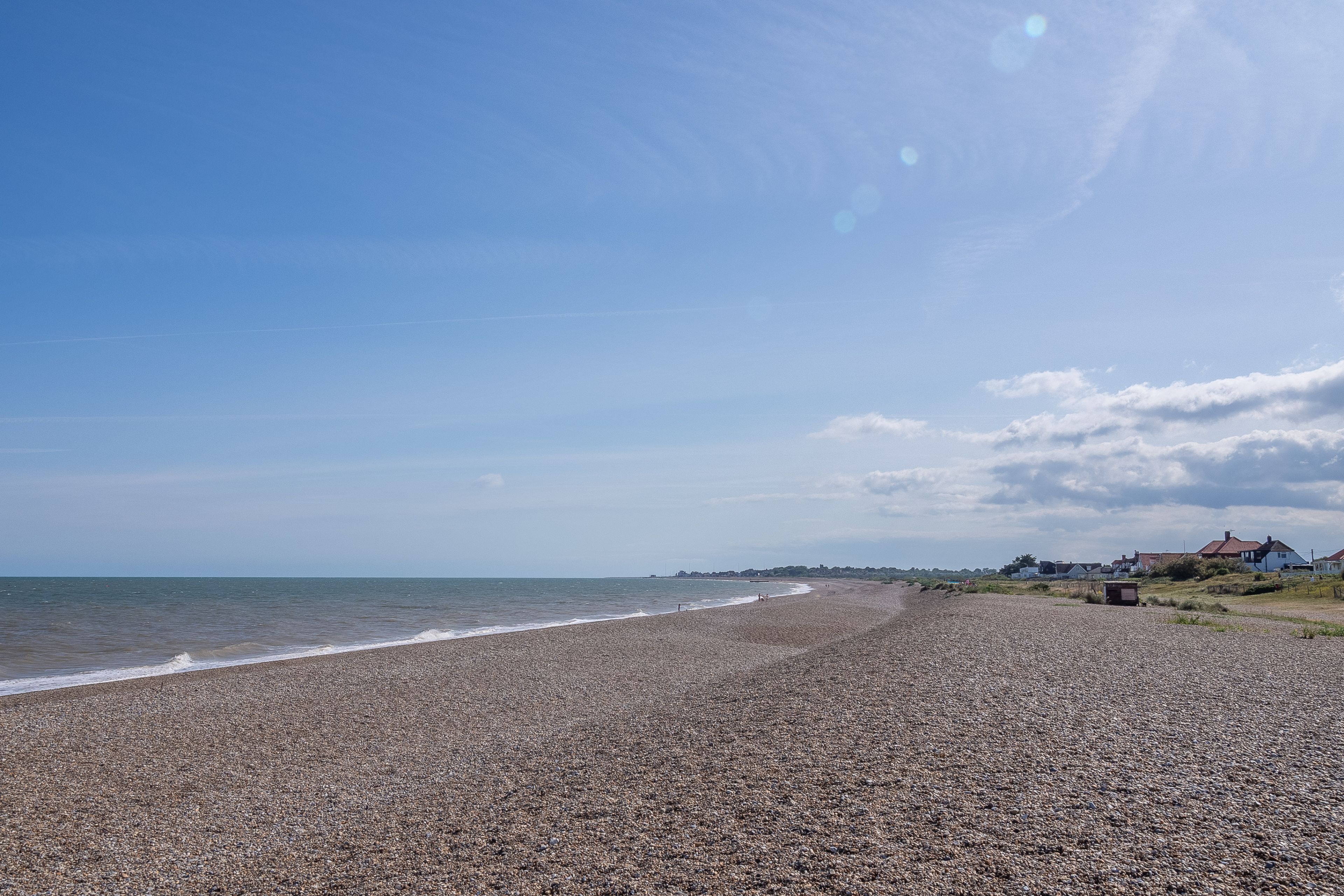 A pebbled beach with houses in the background.