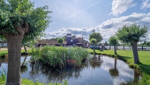 A serene pond with surrounding greenery and a traditional house in the background.