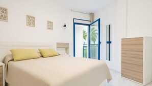 A modern bedroom with a large bed, a wardrobe, and a balcony with a view of palm trees. - Apartamento Las Brisas (Estepona)