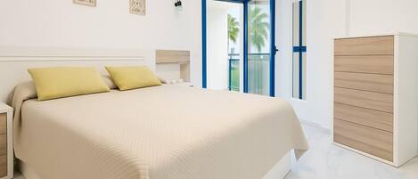 A modern bedroom with a large bed, a wardrobe, and a balcony with a view of palm trees.