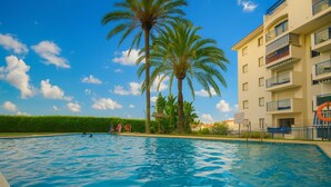 A swimming pool with palm trees and a building with balconies. - Apartamento Las Brisas (Estepona)