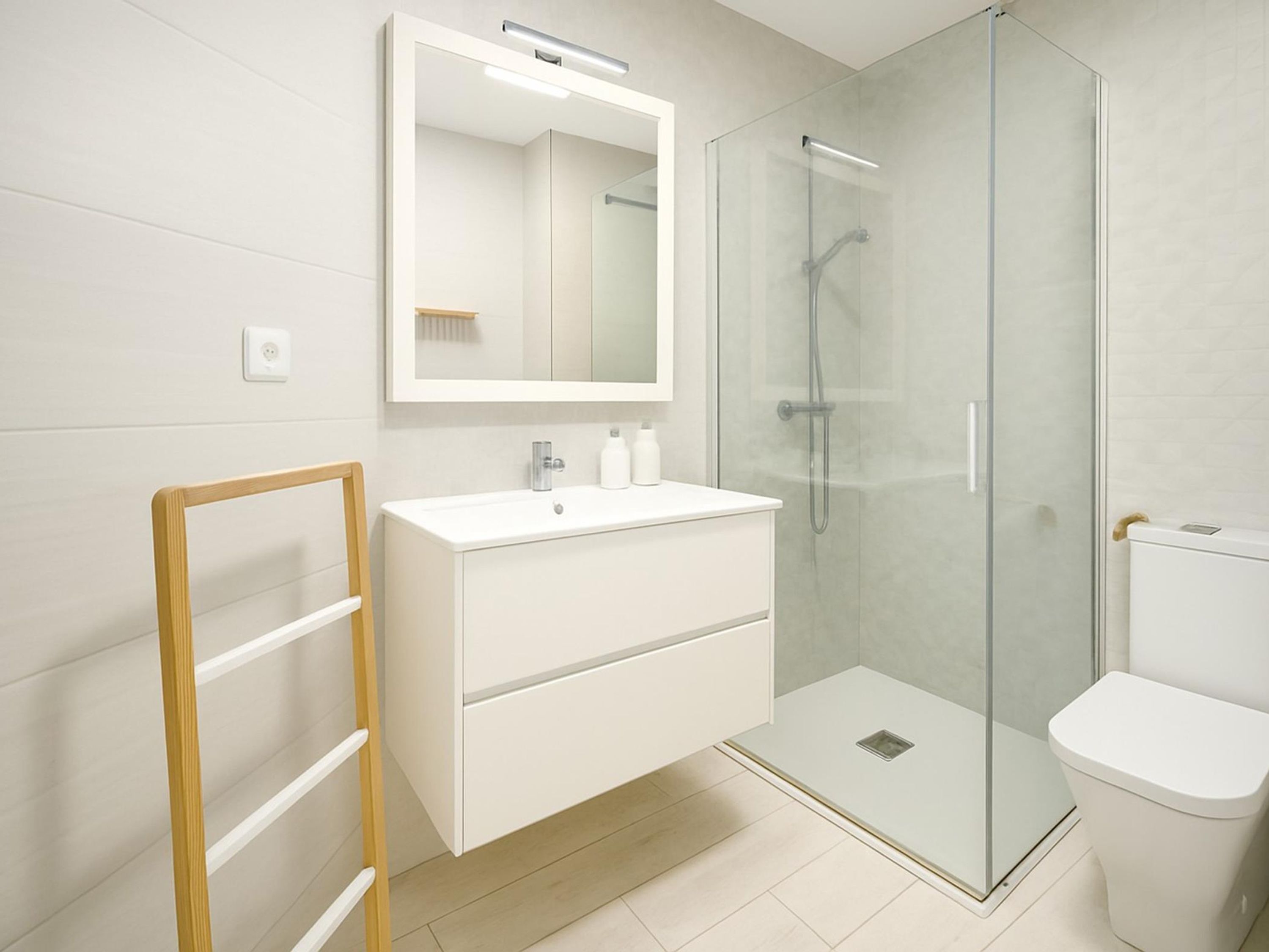 Une salle de bain moderne avec une douche à parois de verre, un meuble-lavabo blanc et une échelle en bois.