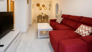 A modern living room with a red sofa, a white coffee table, and a flat-screen TV on a white stand. - Apartamento Las Brisas (Estepona)