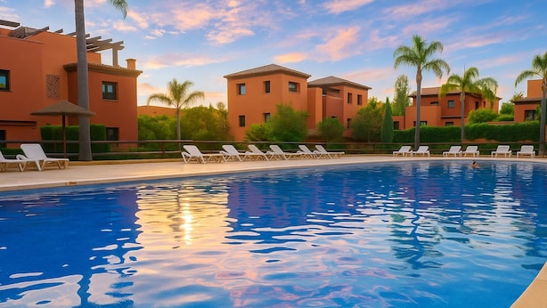 A swimming pool with lounge chairs and a building in the background. - Apto Casares Golf Playa (Casares)