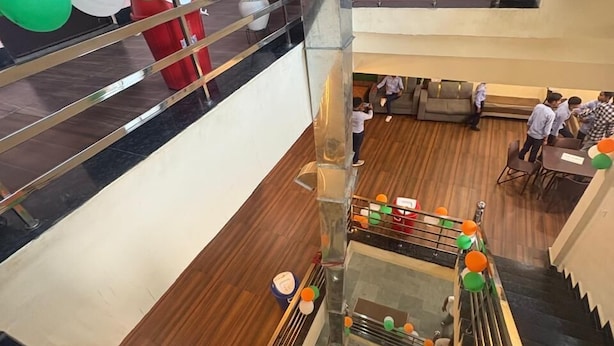 Un atrio de varios niveles con una escalera central, barandillas de vidrio y una zona de estar con mesas y sillas.