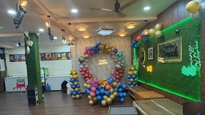 Un área de recepción con suelo de madera, una pared verde con luces de neón y un arco de globos de colores.