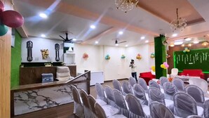 Un salón de conferencias con filas de sillas, un mostrador de recepción y un escenario decorado con globos.