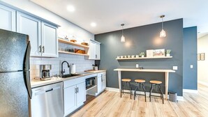 Une cuisine moderne avec des armoires blanches, un four encastré et un plan de travail en bois. Deux suspensions lumineuses sont fixées au-dessus du bar.