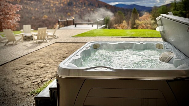 Un bain à remous avec vue sur les montagnes et un espace patio aménagé avec des chaises et une table.