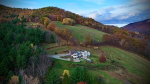 Une grande maison dotée d’une allée spacieuse et de plusieurs garages, entourée d’un paysage verdoyant et vallonné, où les arbres arborent les couleurs de l’automne.