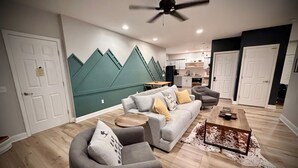 Un salon moderne avec un canapé gris, des fauteuils, une table basse et un ventilateur de plafond.