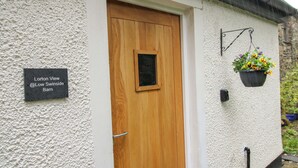 A white textured wall with a wooden door and a hanging flower pot. A sign reads "Lorton View @ Low Swinside Barn".