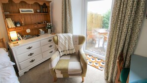 A cozy bedroom with a wooden dresser, a chair, a desk, and a large window with curtains.