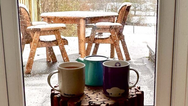 A wooden table and chairs outside a window with a snowy landscape view.