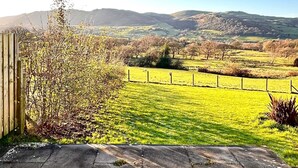 A rural landscape with a fenced field, a wooden structure, and distant hills.