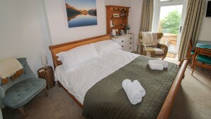 A neatly arranged bedroom with a bed, a chair, a small table, and a window with curtains.