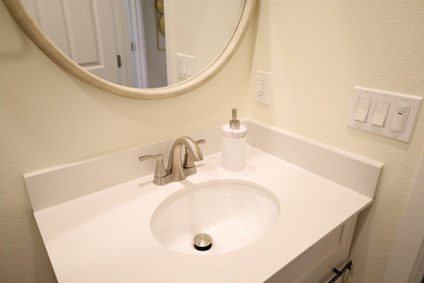 Une salle de bain avec un lavabo blanc, un miroir rond et un robinet.