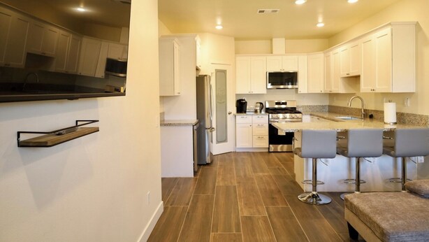 A modern kitchen with white cabinets, a stainless steel refrigerator, a built-in oven, and a bar area with bar stools. - 2-bedroom guesthouse in Riverside. Centrally located near CBU,Parkview and 91fwy (Riverside)