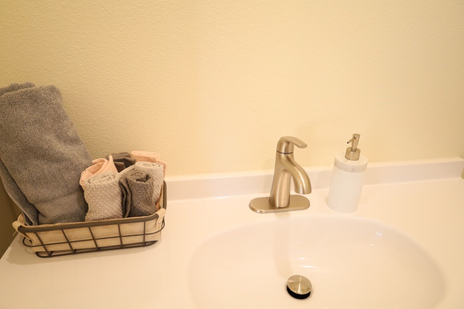 Un lavabo de salle de bain avec un porte-serviettes où sont pliés des serviettes, un robinet et un distributeur de savon.