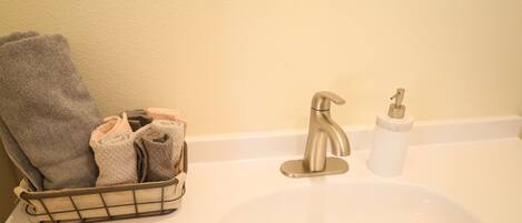 Un lavabo de salle de bain avec un porte-serviettes où sont pliés des serviettes, un robinet et un distributeur de savon.