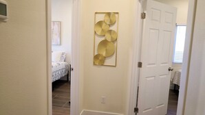 A hallway with a bed in the background, a door on the right, and a wall-mounted decorative piece. - 2-bedroom guesthouse in Riverside. Centrally located near CBU,Parkview and 91fwy (Riverside)