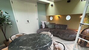 Une pièce avec une table ronde, des fauteuils confortables, un canapé et une plante en pot.