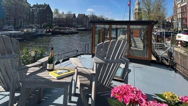 Cubierta de barco con sillas, una botella de champán y flores.