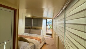 A narrow hallway leading to a bedroom with a bed, a chair, and a view of the outdoors. - Atoll Villa (Hulhumalé)