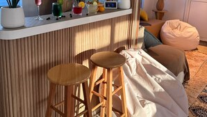 A modern kitchen with a wooden bar counter, two stools, and a view of the city. - Atoll Villa (Hulhumalé)