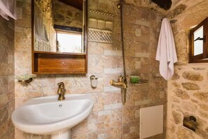 A bathroom with a stone wall, a white sink, a mirror, a shower, and a towel hanging on the wall. - Villa Myli Natural Paradise, quiet, unique, and 10 minutes from town center. (Mili)