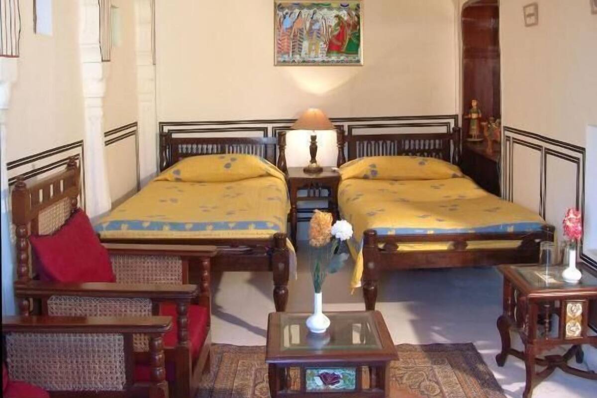 A room with two wooden beds, a red sofa, a small table, and a decorative rug.