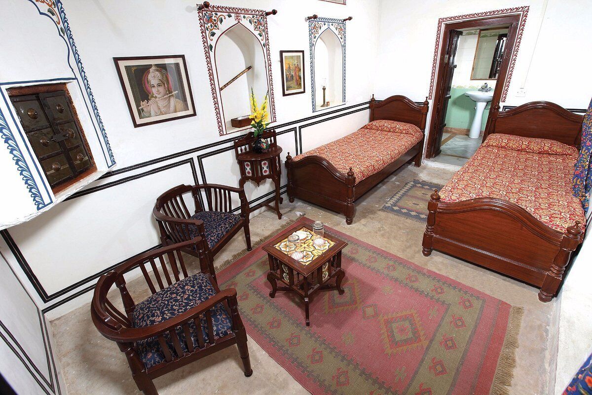A traditional room with two wooden beds, a small table, two chairs, and a mirror.