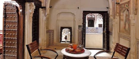 Una habitación con paredes ornamentadas, una mesa redonda con sillas y una vista a través de un arco.