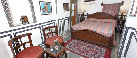 Une chambre traditionnelle avec un lit, deux chaises, une petite table et un miroir.