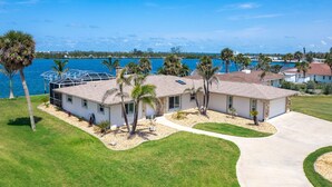 A two-story house with a large front yard, palm trees, and a view of the water.
