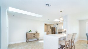 A modern kitchen with a central island, white cabinetry, and a dining area with chairs.