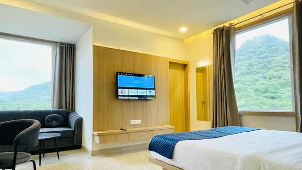 A hotel room with a bed, a sofa, a TV, and a view of the outdoors. - Dhairya Garh  (Udaipur)