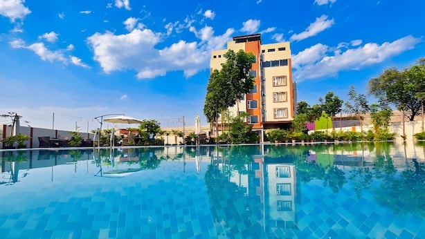 Una piscina con agua azul cristalina, rodeada de vegetación y edificios.