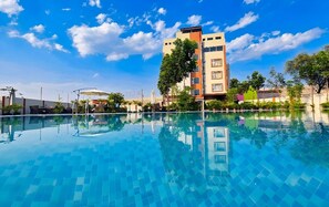 A swimming pool with clear blue water, surrounded by greenery and buildings. - Zuke Garden & Resort (Purulia)