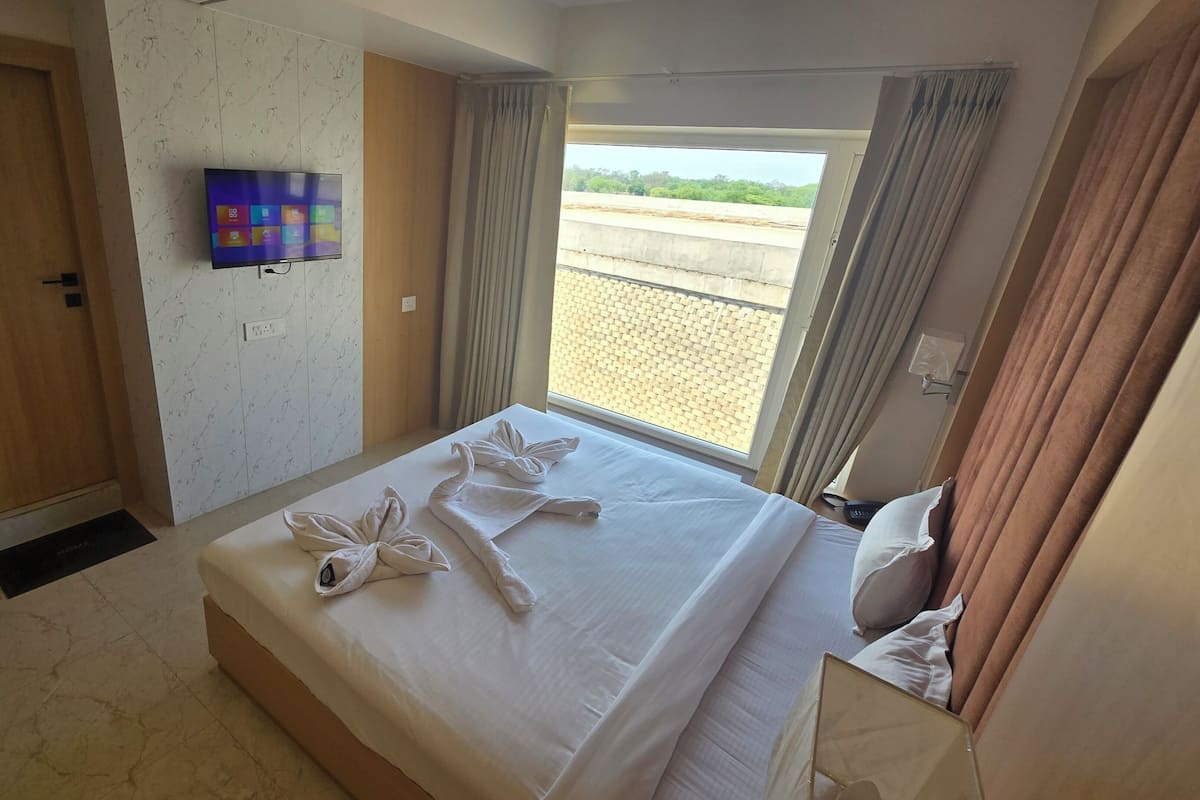 A hotel room with a bed, a TV mounted on the wall, a window with curtains, and a view of the outside.