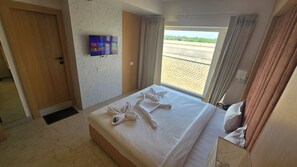 A hotel room with a bed, a TV mounted on the wall, a window with curtains, and a view of the outside. - Zuke Garden & Resort (Purulia)