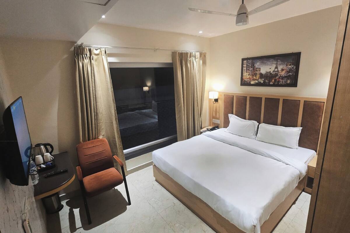 A hotel room with a bed, a desk with a chair, a television, and a window with curtains.