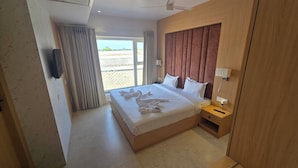 Habitación de hotel con cama, mesita de noche, televisor montado en la pared y ventana con cortinas.