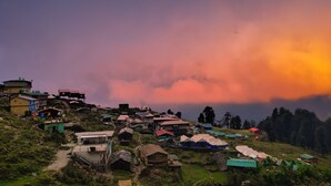 A hillside village with various buildings, including houses and a larger structure on stilts. - RIVER SIDE CAMP CHOPTA  (Pokhri)